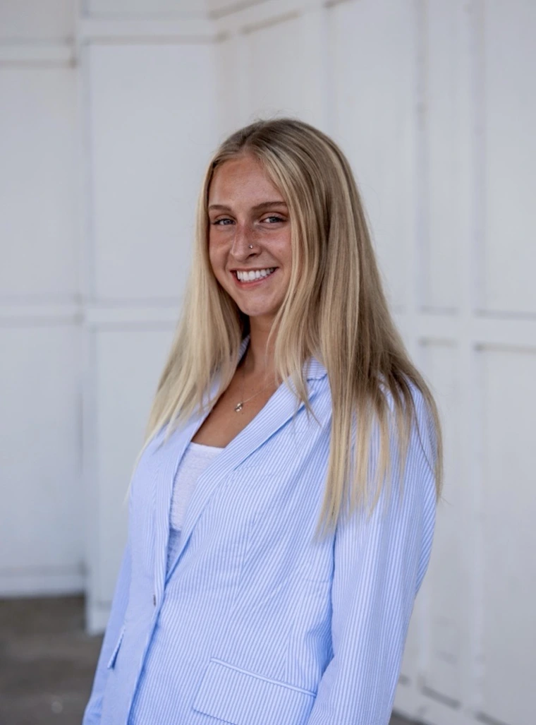 A white woman with blonde hair in a blue suit. She is smiling. 